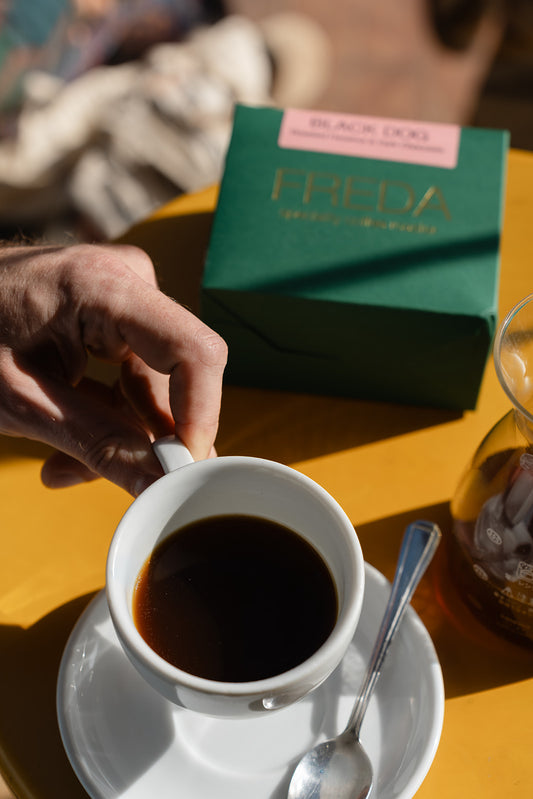 Hand holding coffee cup with Freda Coffee packaging in background, taken in Bond Street Coffee, Brighton Best Cafe, Sussex